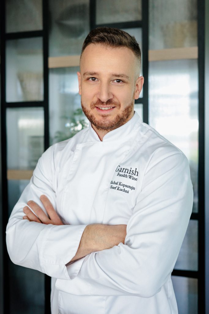 mężczyzna w białym stroju kucharza, z założonymi rękami, uśmiechnięty