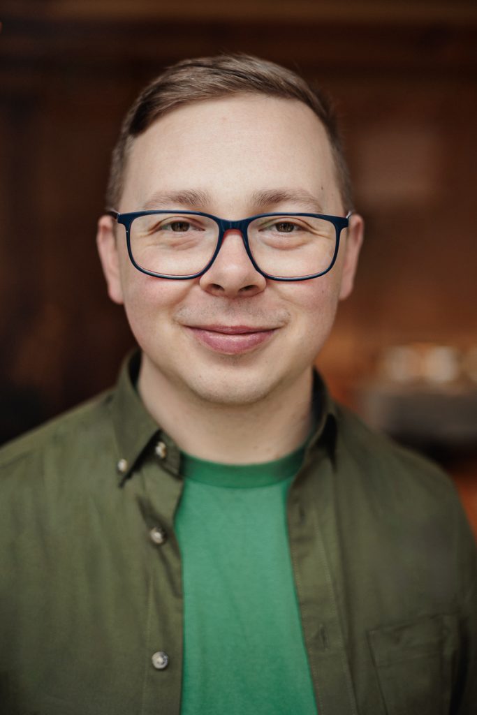 młody mężczyzna w czarnych okularach, ubrany w zielony t-shirt i koszulę khaki